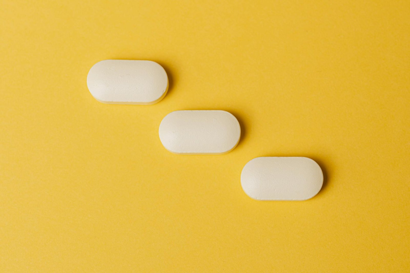 Three white pills arranged on a vibrant yellow background, viewed from above.